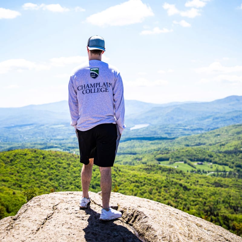Champlain College student standing on a mountain overlooking the Champlain valley