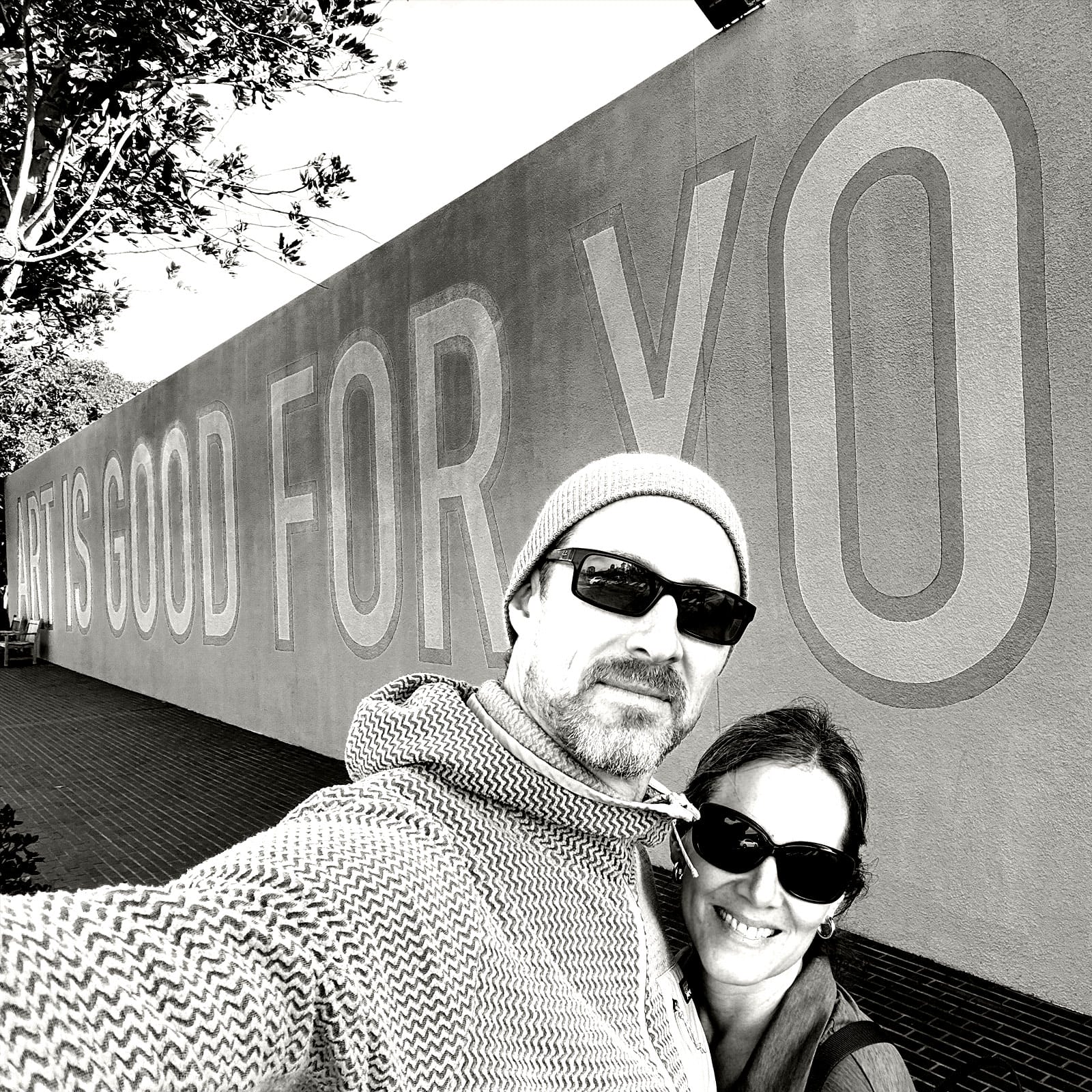 Me and my wife standing in front of a wall that says Art is Good for You
